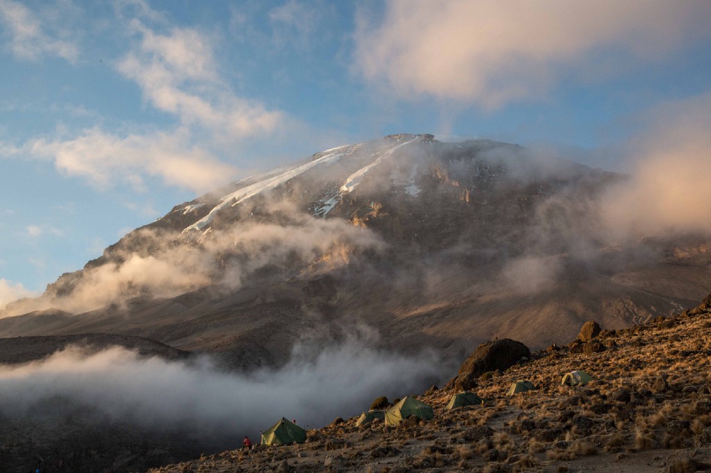 Destinations Worth Dreaming Image: Morning mist is beginning to burn off as the sun rises on a mountain. Green tents dot the landscape.