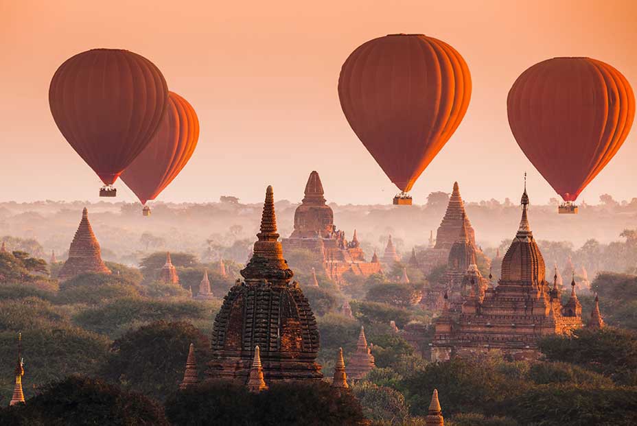 Destinations Worth Dreaming Image: Four rust coloured hot-air balloons float past the Myanmar skyline.
