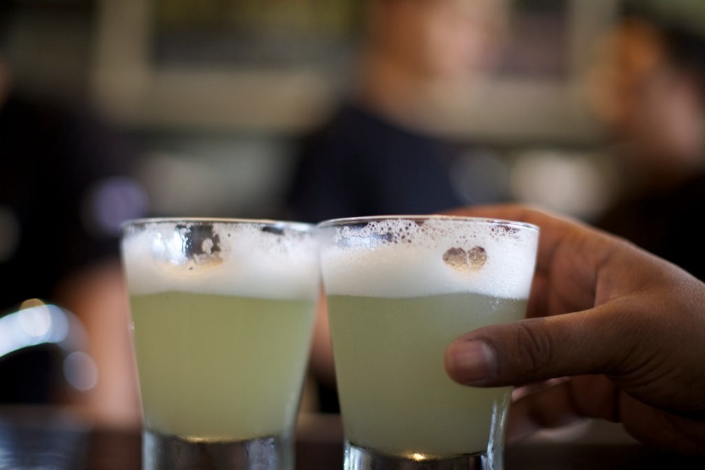 Visit Peru Image: A hand reaches for one of two Pisco sours on a table.