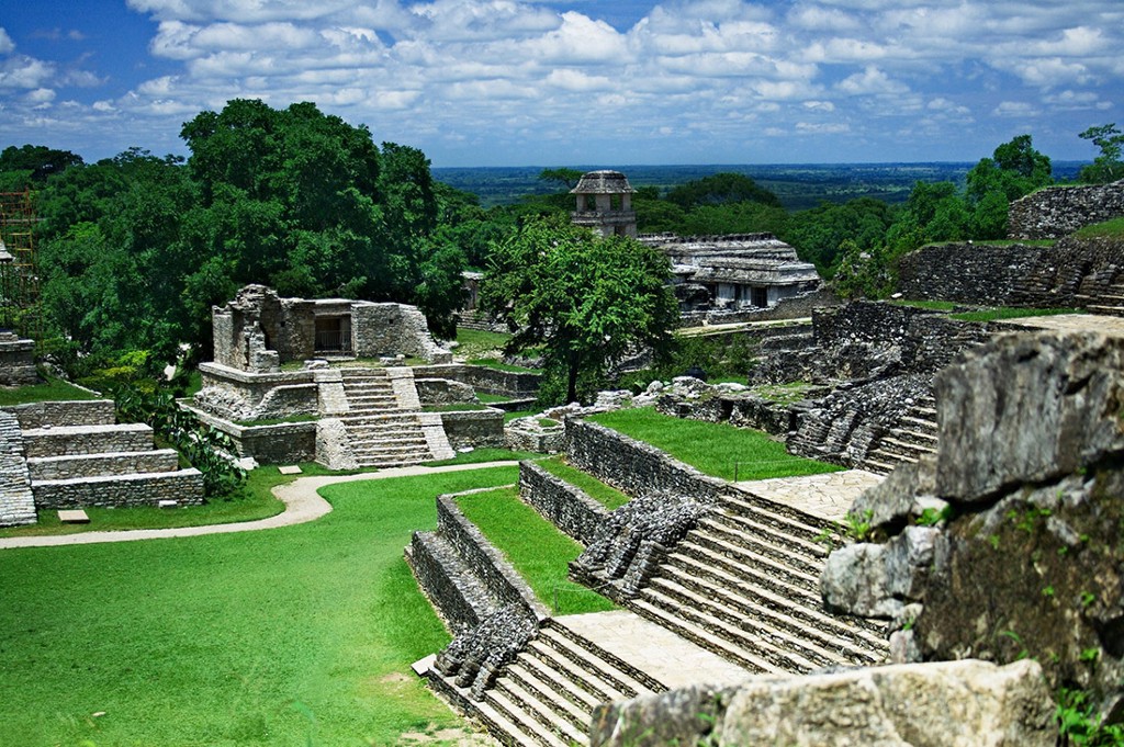 Central and South American Ruins Image: Belize's ancient city is a series of timeworn and muted greys, juxtaposed by green lawns, and jungle trees. A blue sky and white clouds complete the scene.