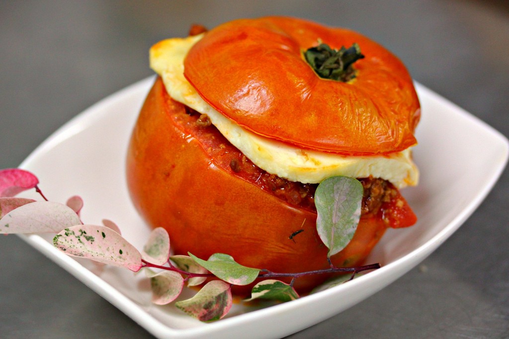 Visit Peru Image: A red rocoto pepper sits on a white dish. The cap of the pepper was cut off, and has been placed back on top of the filled pepper and cheese.