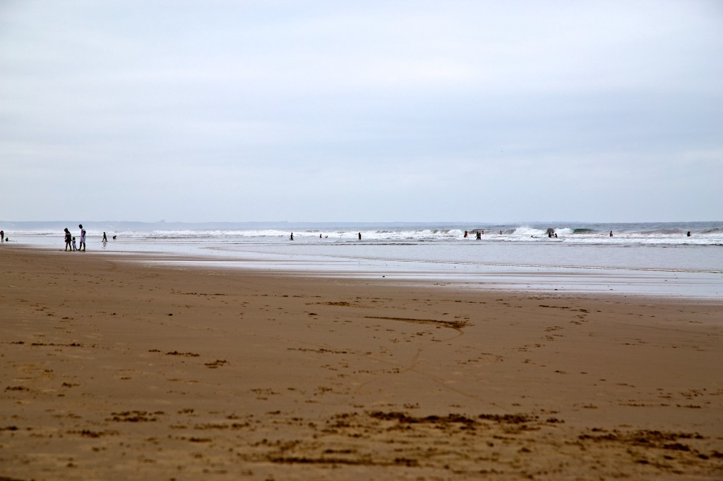 Best Surfing Beaches: People are enjoying the sand and surf of a long and wide stretch of beach.
