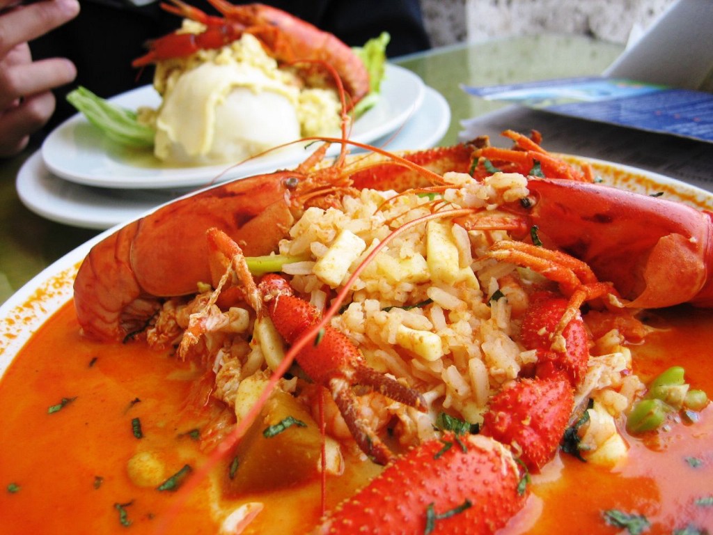 Visit Peru Image: The vibrant red seafood soup is piled onto a white dish; a generous scoop of rice has been placed in the middle of the dish.