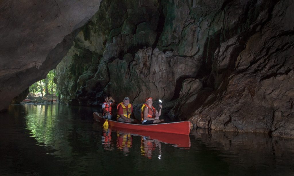 Cave Floating Image: Three people in a canoe pass between the rocky walls of a cave.