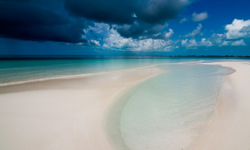 Are Cuba's Beaches Nice Image: A vibrant beach with clear waters, and a beautiful dark blue cloudy sky.