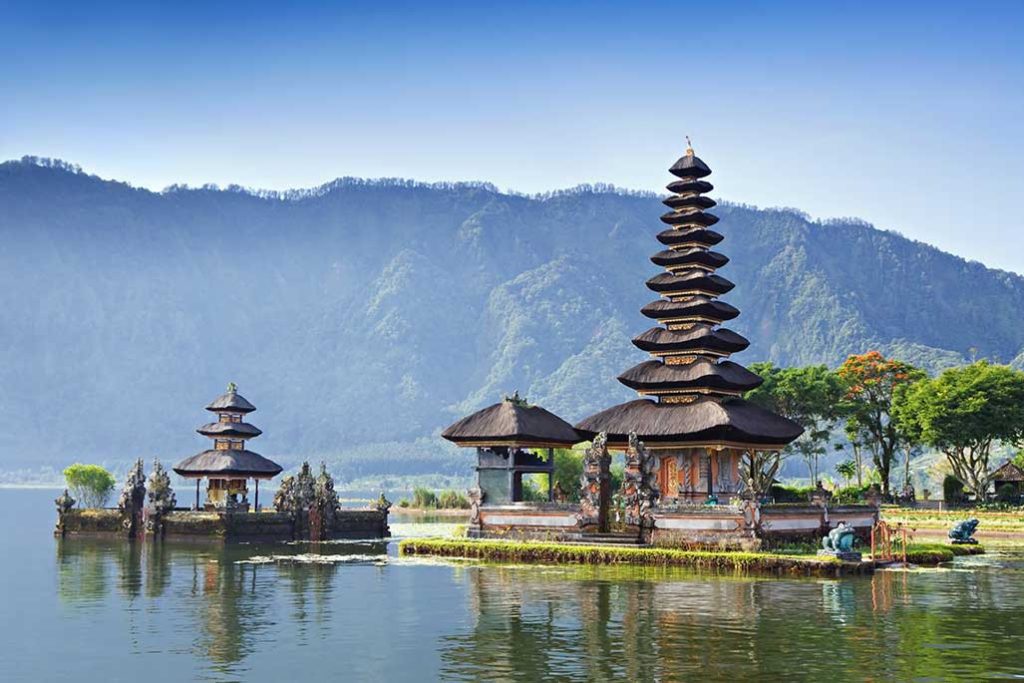 Destinations Worth Dreaming Image: A beautiful pagoda has 11 tiers which from a graceful point. To the immediate left is smaller structure. Further left is a three-tiered pagoda. This scene overlooks water and has a green mountain range in the background.