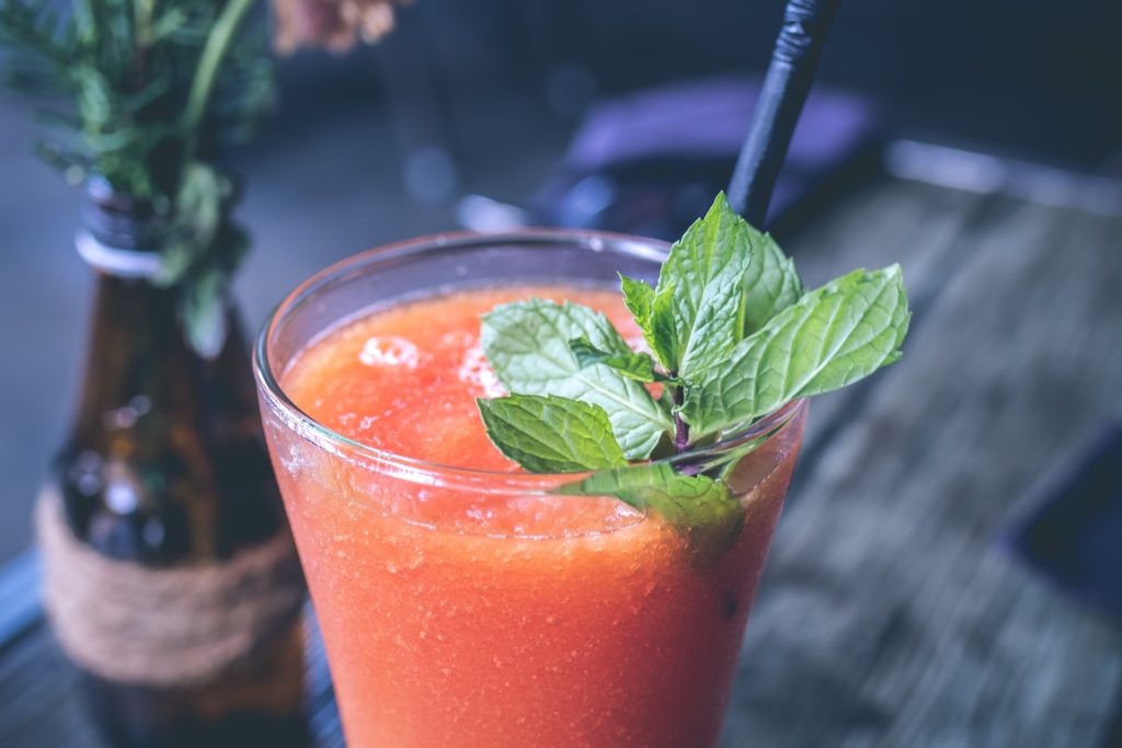 Costa Rican Foods: An ice cold glass of carrot and orange juice is adorned with a black straw and green mint leaf. An old bottle filled with flowers sits adjacent.