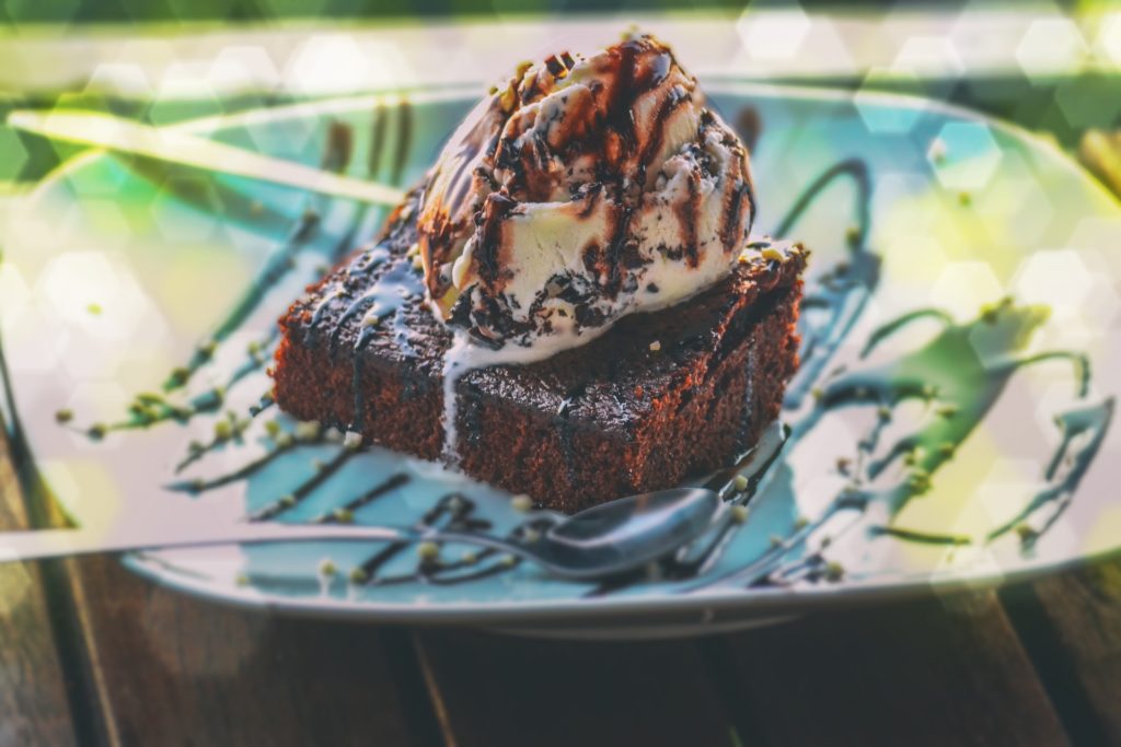 Costa Rican Foods Image: A brownie sits on a plate, and is topped with a scoop of ice cream, and a chocolate drizzle.