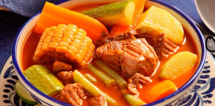 Costa Rican Foods Image: A bowl of olla de carne contains generous chunks of corn cobs, beef, squash and other vegetables swimming in a savory broth. 