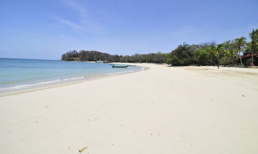 Best Beaches Image: Panama. A beautiful but lonely beach has white sand, blue water and skies, and a boat near the shore. One person can be seen in the distance.