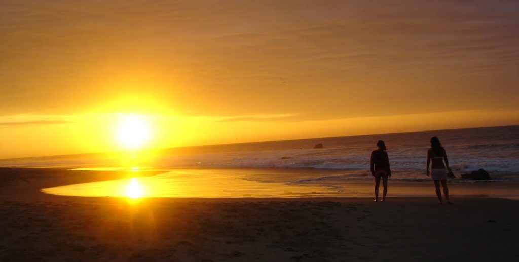 Best Beaches Image: Peru. A golden sunset washes over a Peruvian beach as two onlookers take it all in.