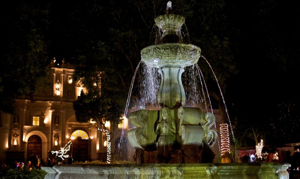 Mayan Image: A fountain and possibly a Spanish-colonial building are illuminated on a dark night.