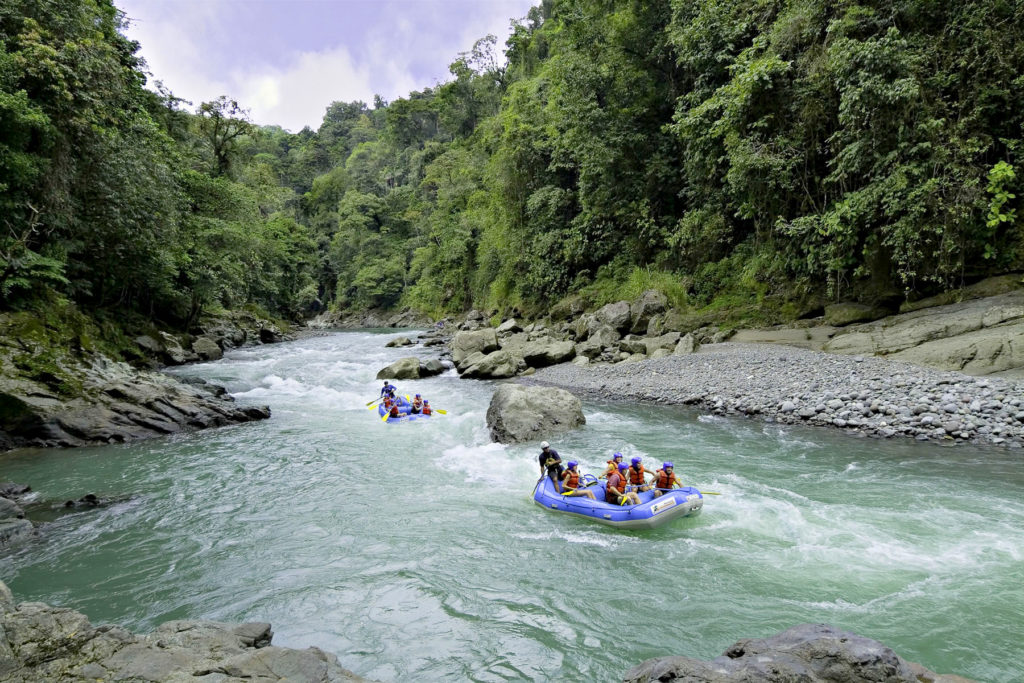 Costa Rica Rafting Image:  Two sets of rafters are in a wide stretch of open water, making their way around large boulders.