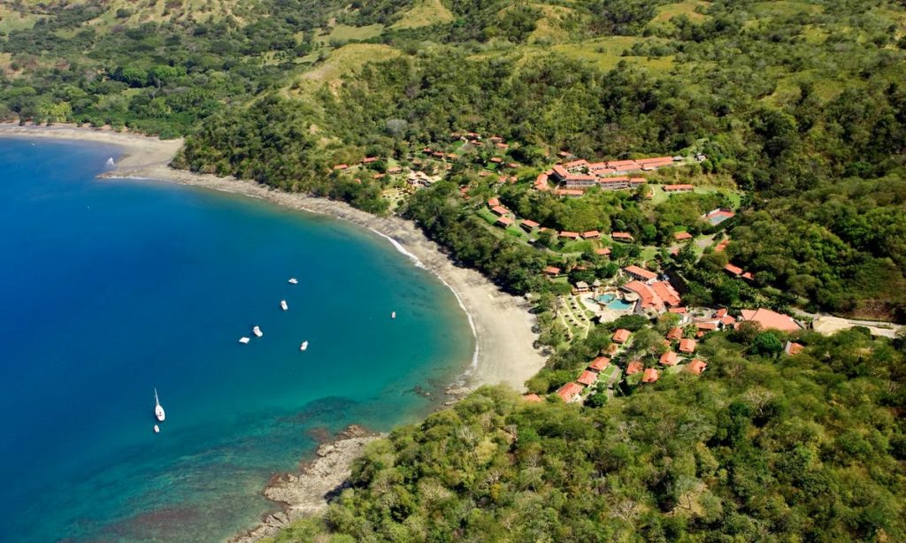 Best Beaches Image: Costa Rica. A small handful of watercraft sail about a pristine blue inlet. Save for the accommodations built into the land, the area is green.