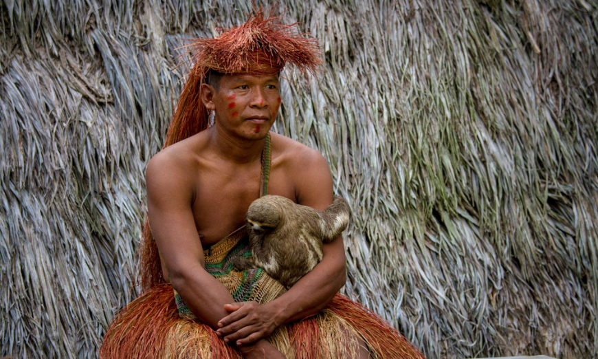 Peru Amazon Image: A Yagua man sits in traditional dress holding a sloth.