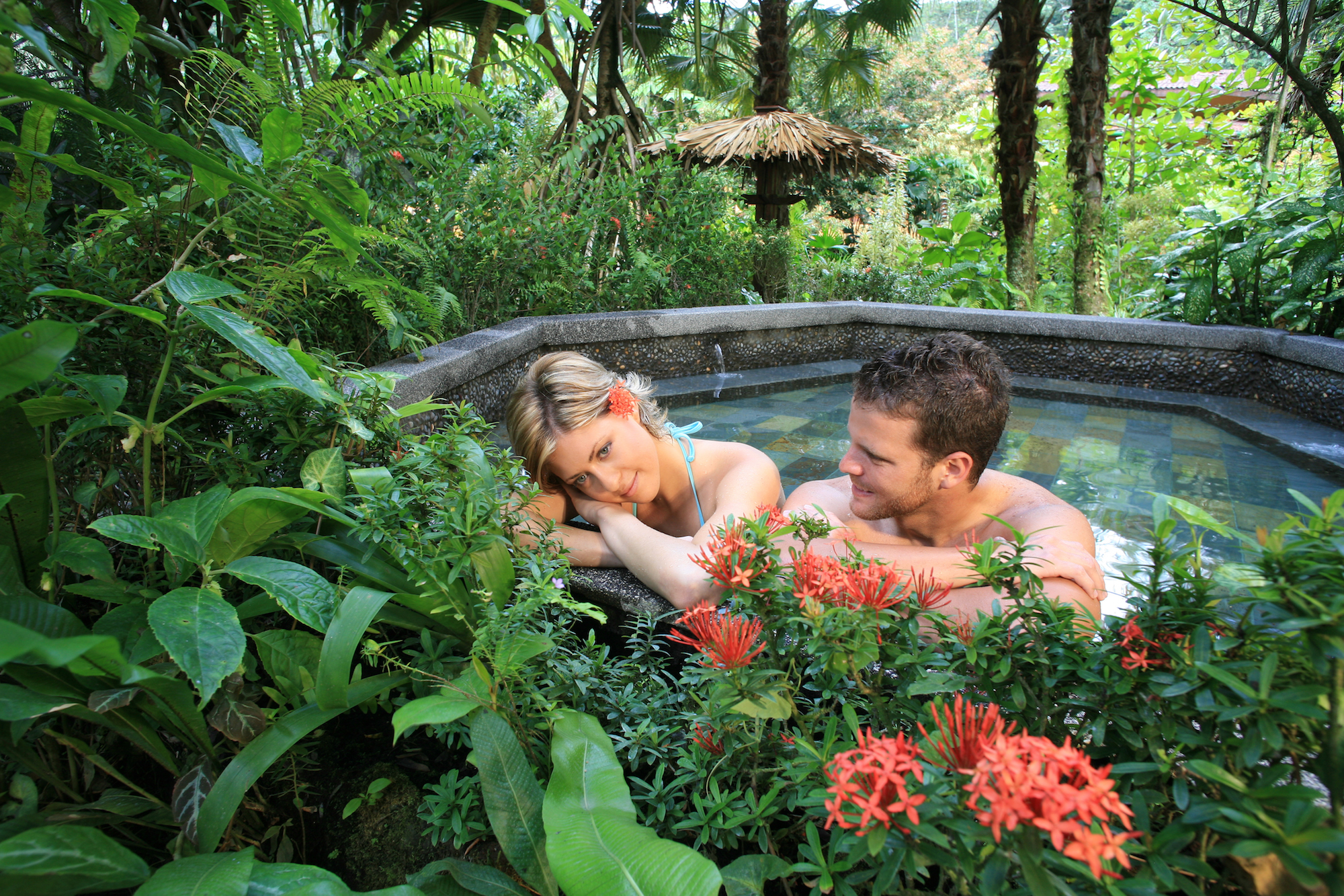 Hot Springs Image: Tabacon Hot Springs Costa Rica. A couple sits in the warm water enjoying each others company, and admiring the ample foliage surrounding them.