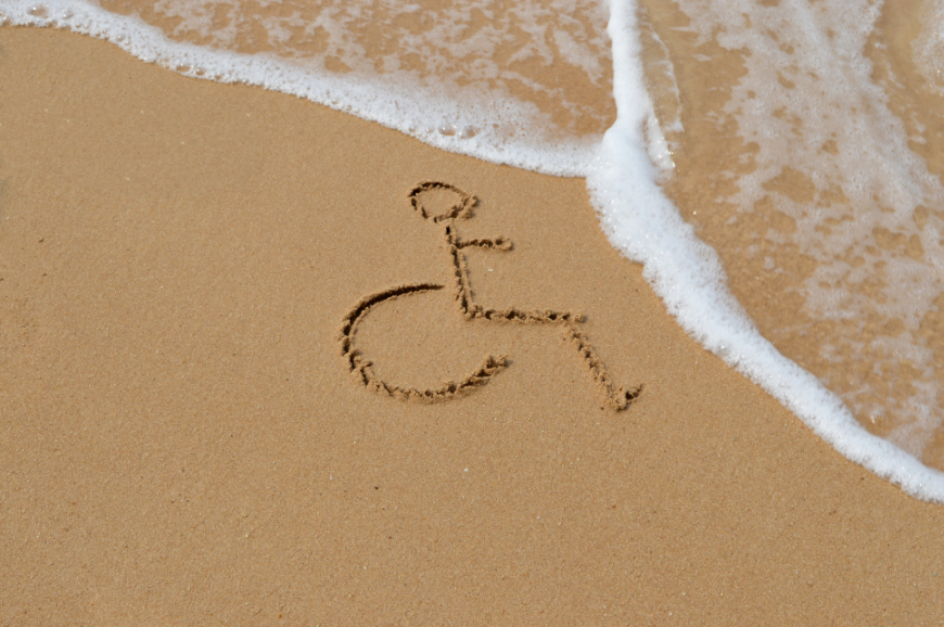 Accessible Travel Image: The accessibility travel of a wheelchair is drawn in the sand as waves flow in. Don't let accessibility needs stop you from going on a family holiday.