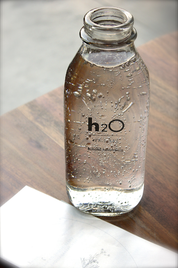 Altitude Sickness Image: A clear glass water bottle in the shape of a milk bottle sits adjacent to a napkin on a wooden table.