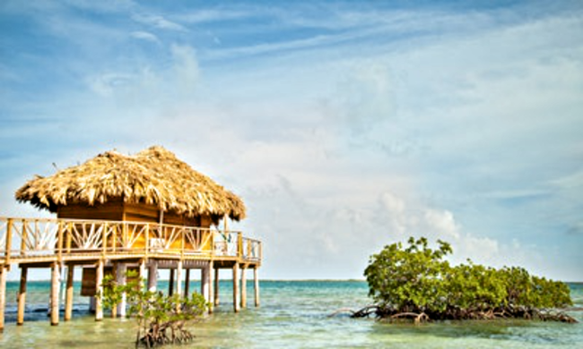 Belize Island Image: A thatched roof overwater bungalow is on stilts.