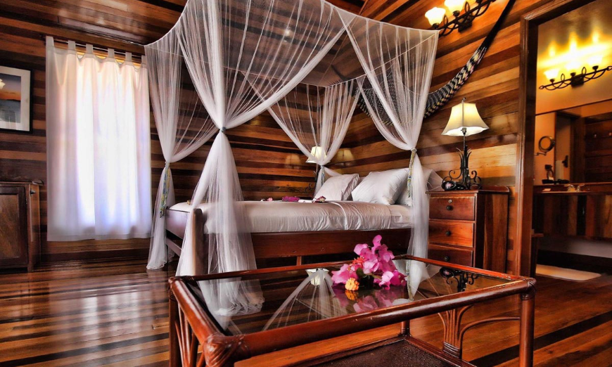 Best Beaches for Swimming in Belize Image: A beautiful wooden room features fuchsia flowers on a glass tabletop, and a four poster canopy bed.