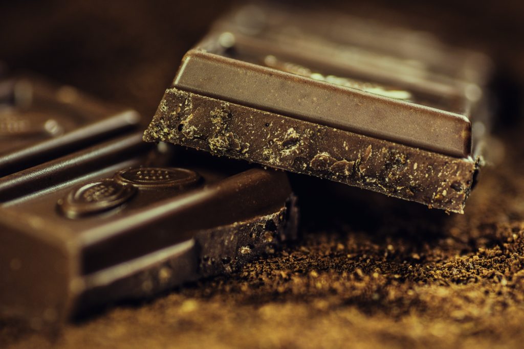Best Chocolate Image: A close-up of a segmented chocolate bar broken, with one layer resting on top of another, and surrounded by coca powder and ground chocolate.