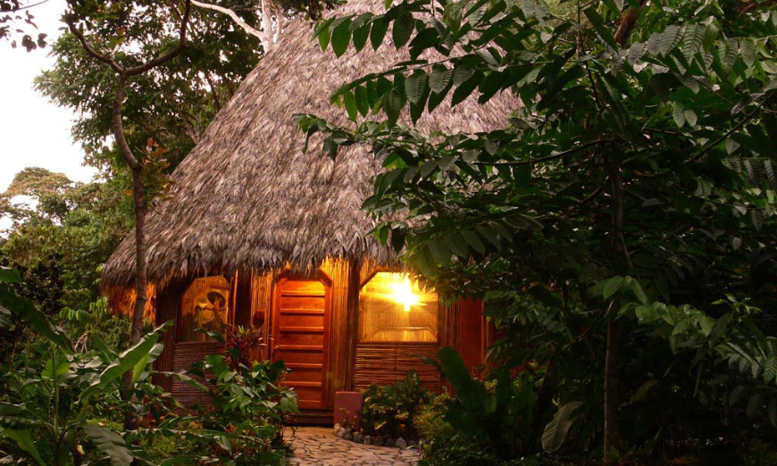Best Eoctourism Lodges Image: A light is shining through the window of a thatched roof bungalow.