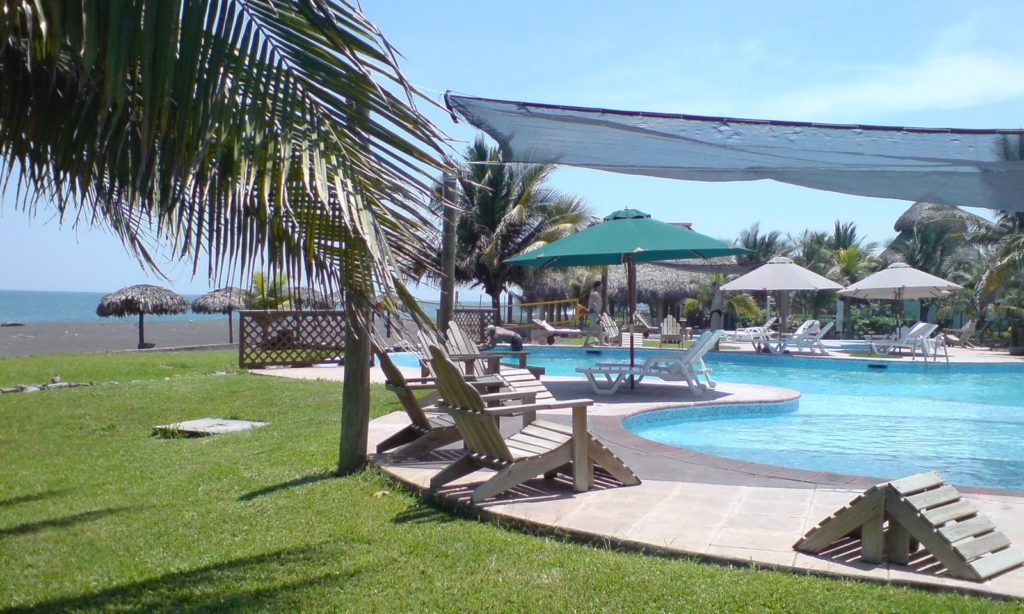 Best Surfing Beaches: Pictured is the hotel's swimming pool, surrounded by lunge chairs, umbrellas, and palm trees. Outside of a wooden gate is an immaculate green lawn which leads down to the black sand beach.