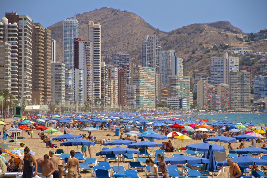 Best Travel Stories Image: A beach is crowded by tourists, their lounge chairs, and beach umbrellas. Skyscrapers block most of the landscape.