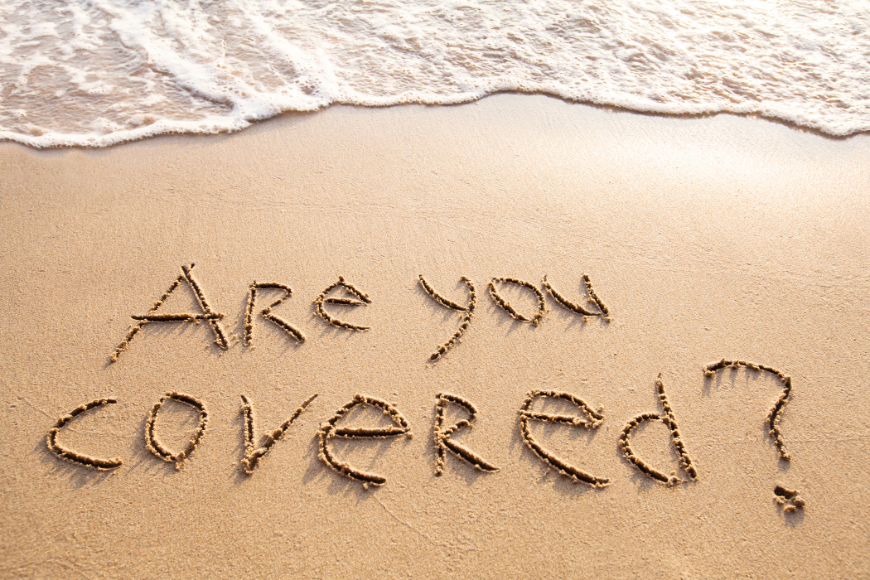 Booking A Vacation Online Image: The question 'Are you covered?' is written in the sand on a beach, with a wave coming in nearby.