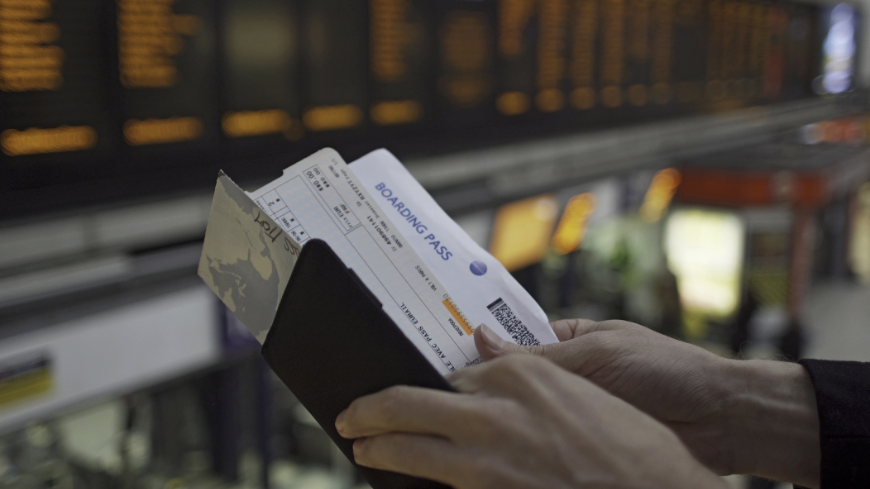 Booking A Vacation Online Image: A person's hands are examining an itinerary, ticket, and boarding pass. 