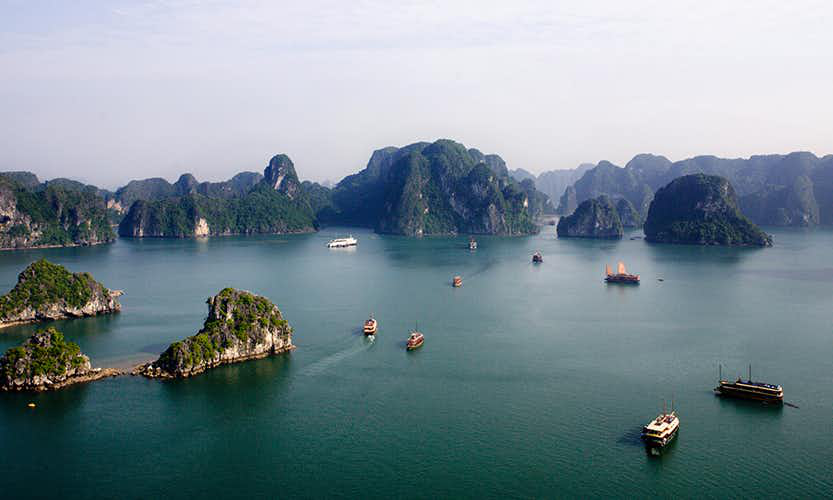 Caving in Vietnam Image: Boats navigate the green mounds and waters of Ha Long Bay.