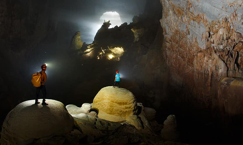 Caving in Vietnam Image: Two people stand on large mounds in the massive Hang Son Doong cave.