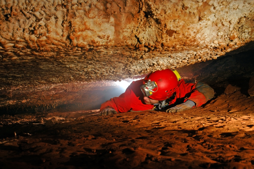 Caving in Vietnam Image: An cave explorer crawls through a narrow passageway.