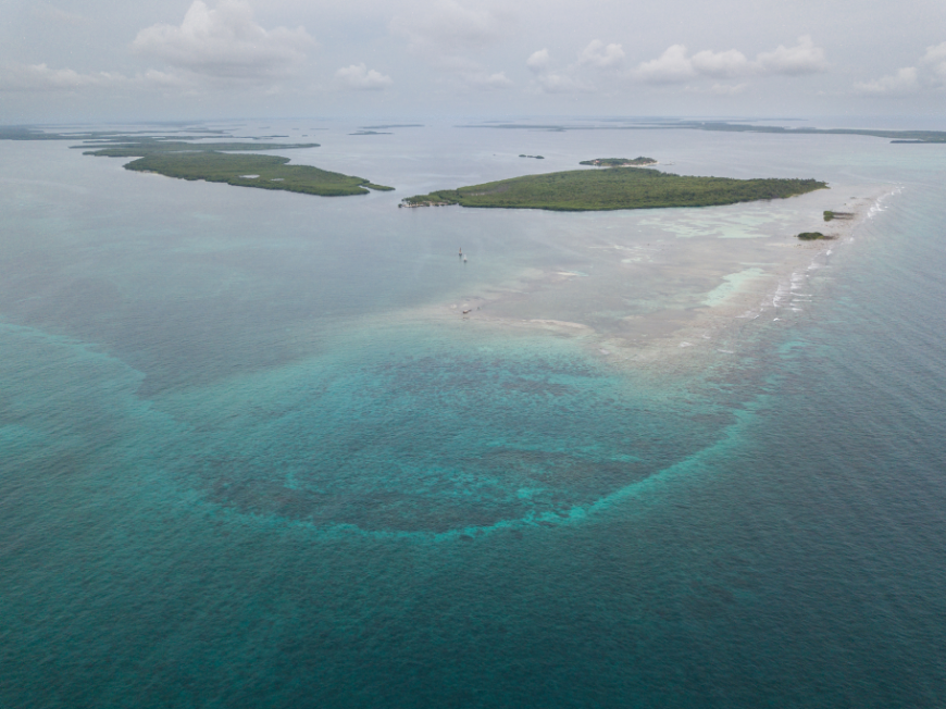 Central America Islands Image: An aerial of lush, green mounds of land, and coral that seems to glow peeking through water.