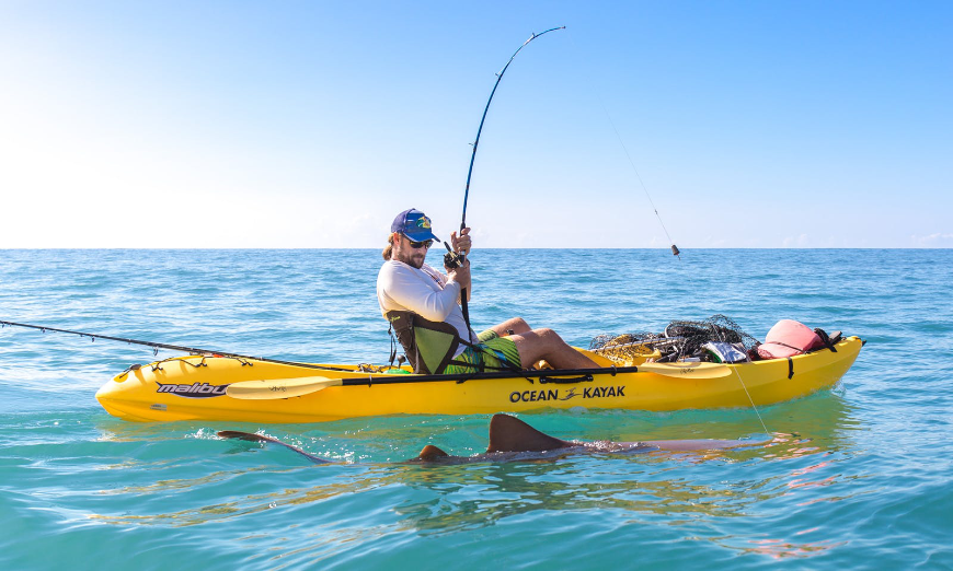 Costa Rica Activities Image: A man with a blue baseball cap sits in a yellow kayak sport fishing. He has caught a shark.