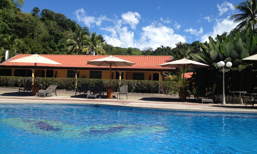 Costa Rica Mother's Day Image: A building sits in the background as the lounge chairs, umbrellas, and swimming pool of Cabinas Espadilla take the focus.