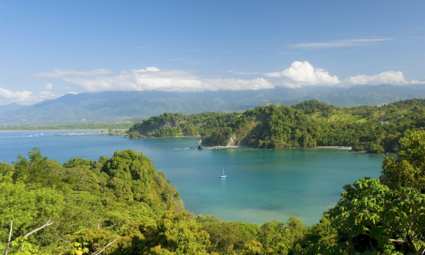 In Costa Rica, a boat sales in an inlet surrounded by trees on a sunny day..