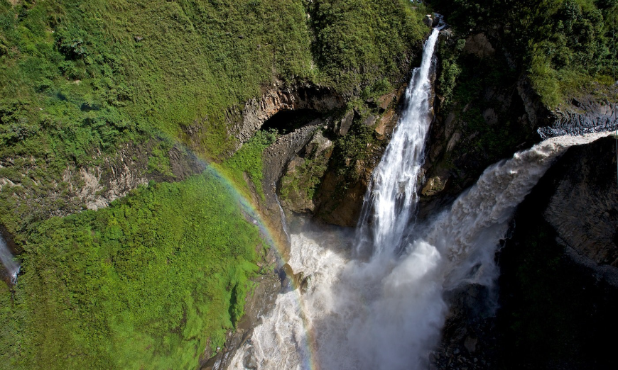 Destination Wedding in Ecuador Image: A rainbow crests over a green mountain with rushing waterfall and raging river.