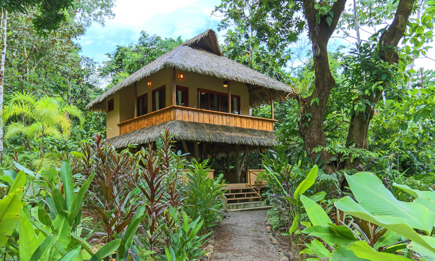 Eco-Friendly Destination Wedding Image: Exterior of Copa del Árbol. A wraparound balcony and thatched roof building sits in the midst of a forest.