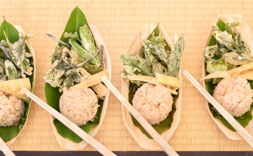 Eco-Friendly Destination Wedding Image: A vegetarian meal including rice and vegetables rests on leaves in a natural container, served with chopsticks.
