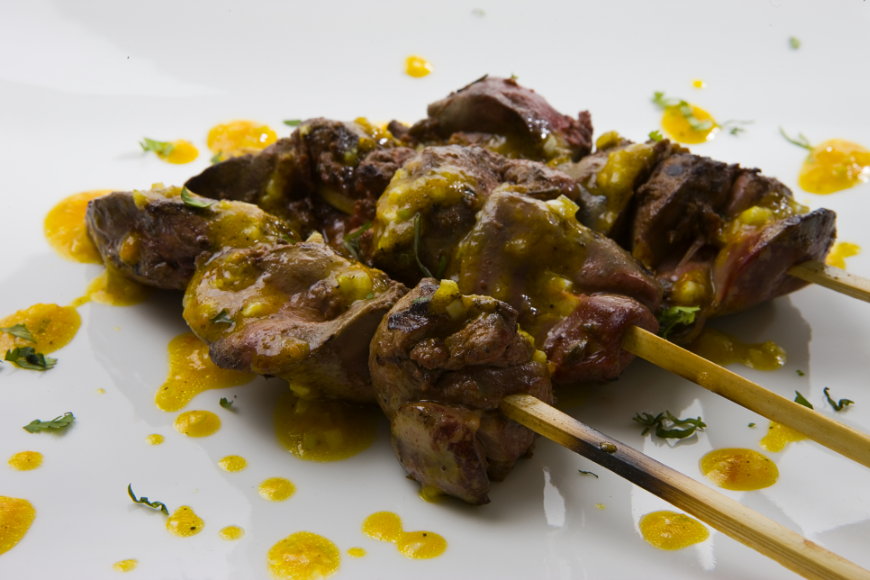 Eat In Peru Image: Three anticuchos are on a white plate drizzled in a golden sauce.