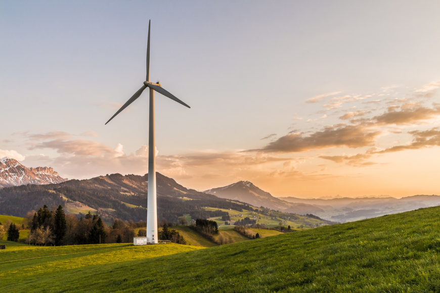 Environmentally Sustainable Tourism Image: A wind turbine sits in the middle of a meadow; in the distance is a mountain.
