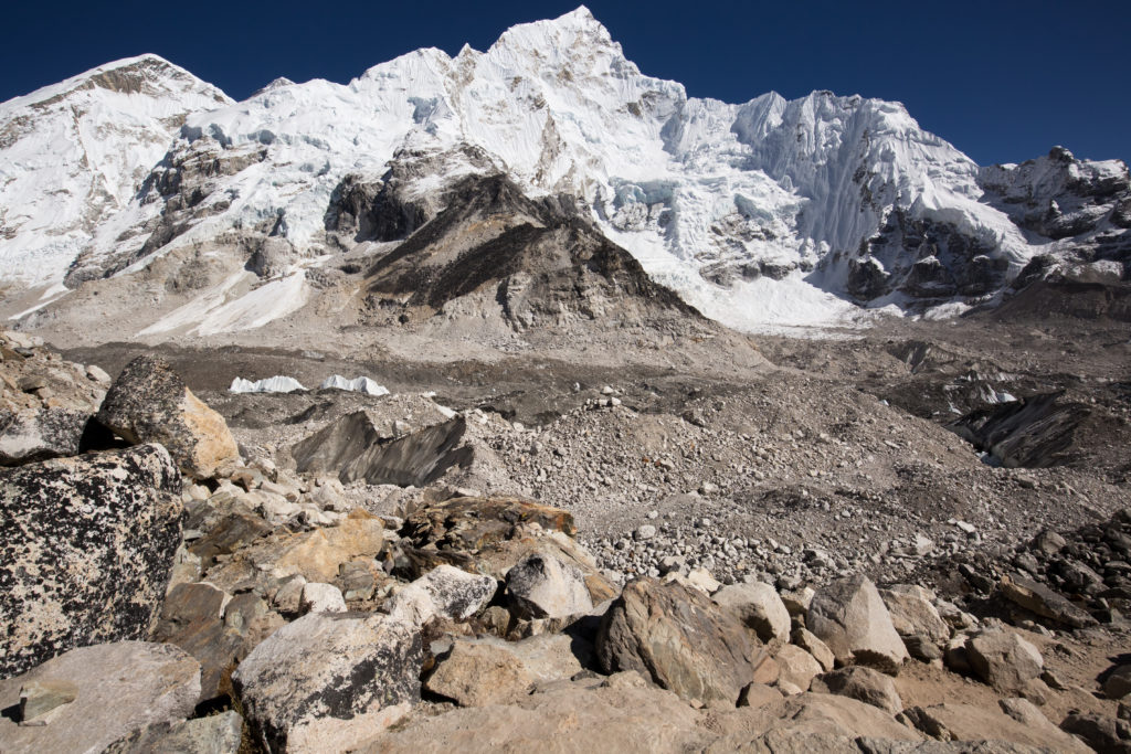 Everest Base Camp Image: From a rocky brown path, we see a larger snow covered peak.