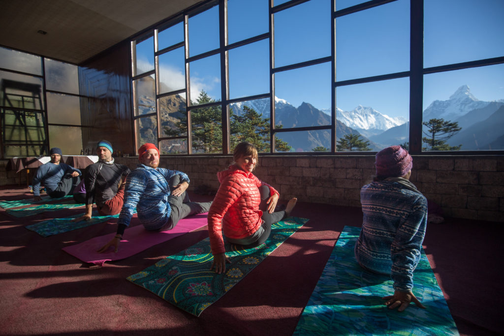 Everest Base Camp Image: Five members of the Everest Base Camp trek do yoga on mats with trees and mountains in the background.