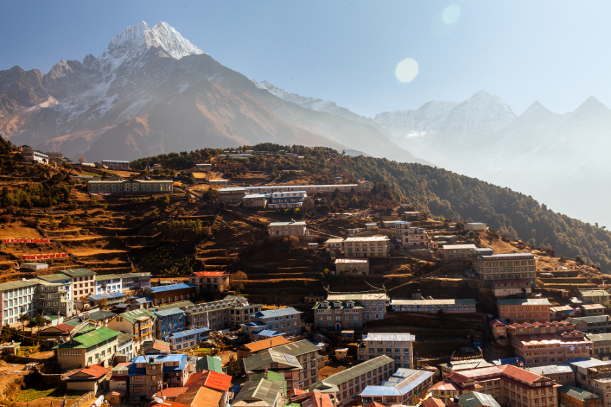 Everest Tattoo Image: Mountains loom over the buildings of Namche Bazaar — shown at a distance.