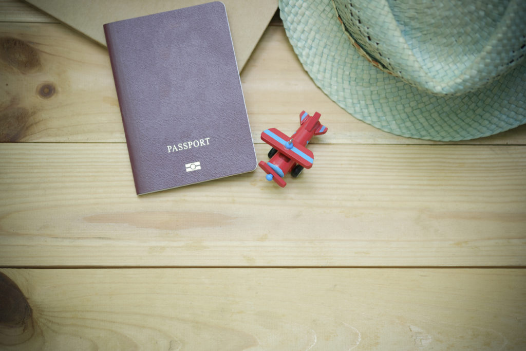 Family Adventure Image: On a wooden floor sits a passport, mint green straw hat, and a red toy plane with blue stripes.