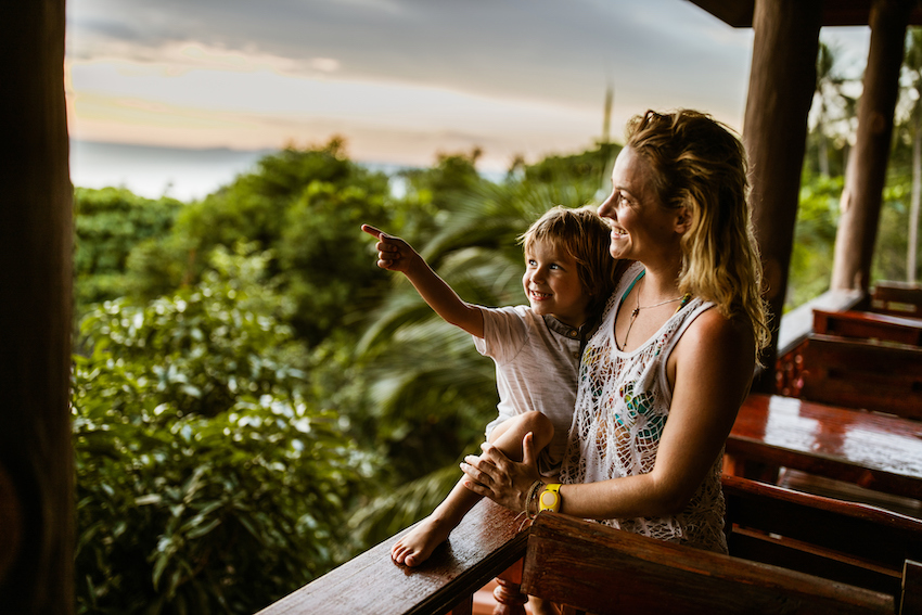 Trip Postponement Image: A mother and child look over a balcony and enjoy their tropical getaway.