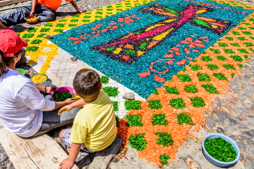 family vacations in belize and guatemala image: A family works on a holy carpet using colored sawdust. 