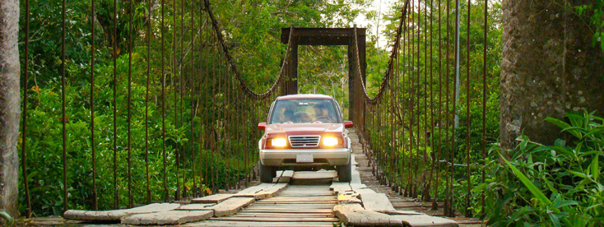 Getting Around in Costa Rica Image: A small SUV or pickup drives over boards placed on a jungle bridge.