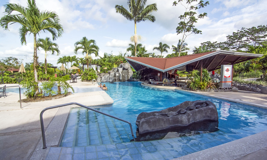 Green Season Image: Sunlight and palm trees grace a pool lounge area.